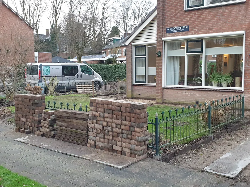 Voortuin met gemetselde keermuur en zwart sierhek langs de stoep