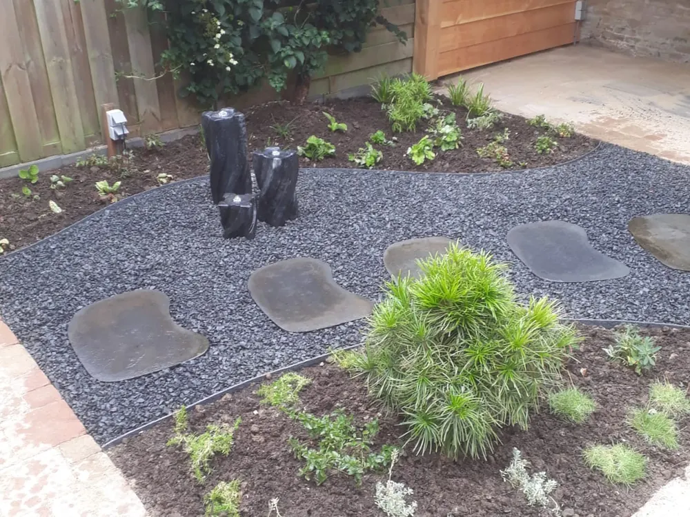 Border met grind, siergrassen en een jonge boom langs een pad